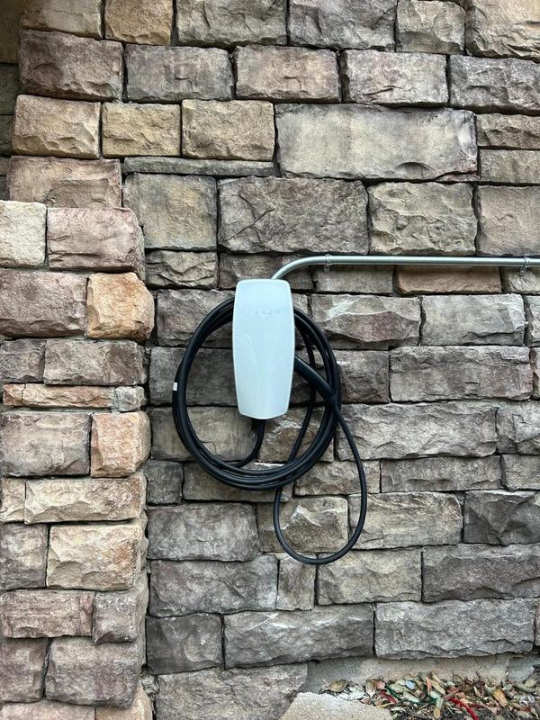 White wall-mounted EV charger with its cable coiled, on a stone wall