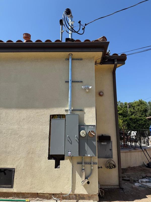 New electrical service mast, meter and main panel on the stucco wall of a house with a tile roof