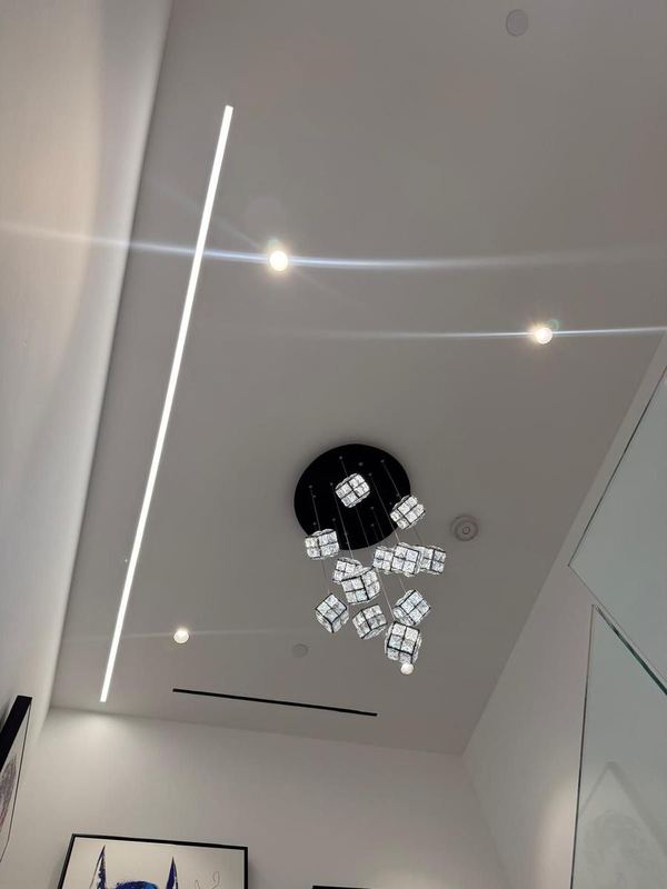 High ceiling with a linear light strip, recessed lights and a crystal chandelier