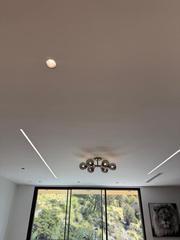 Living room ceiling with linear light strips, recessed lights and a globe fixture above a window to a green hillside